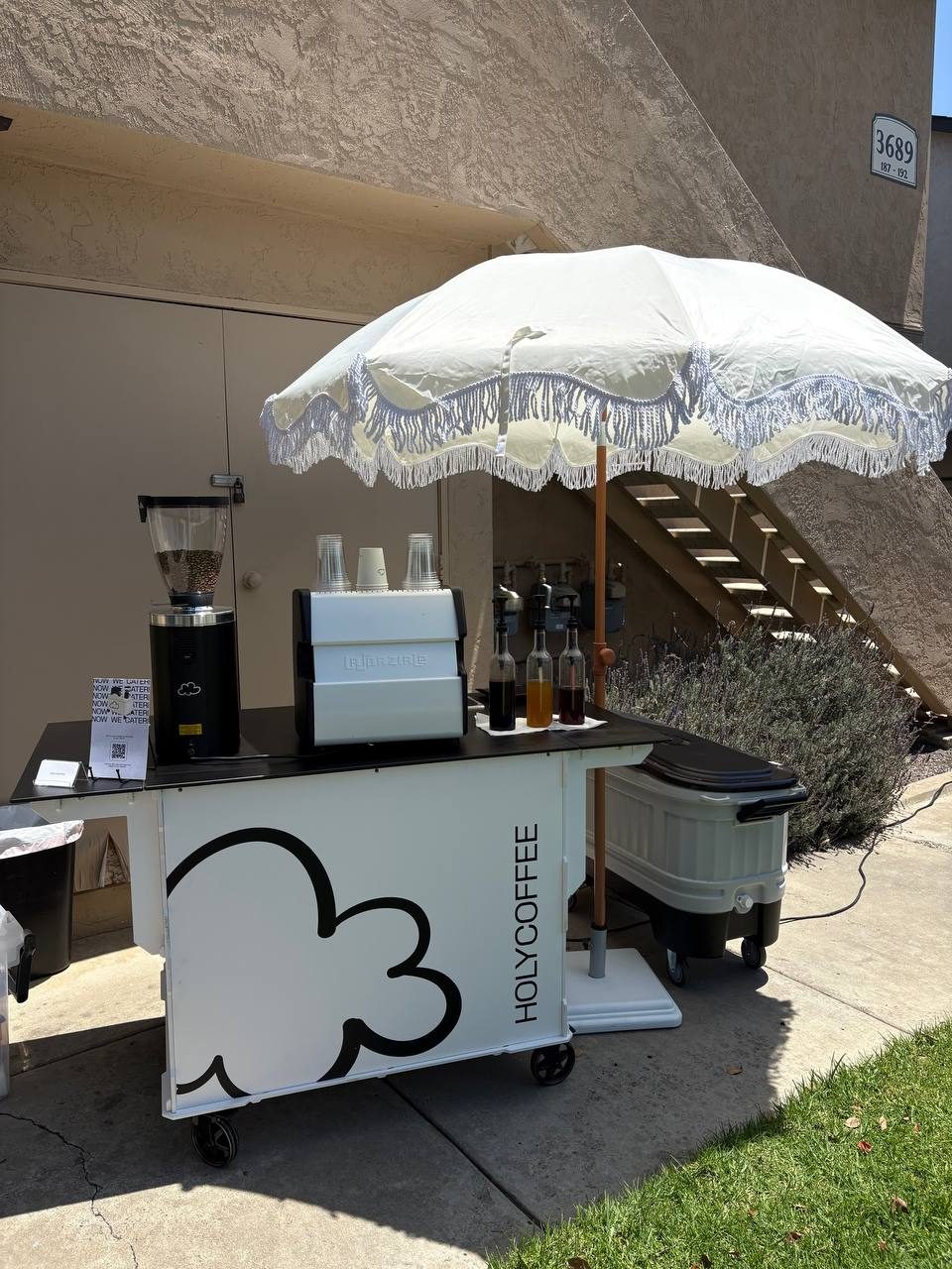 Holy Coffee cart with a white fringed umbrella on a lawn