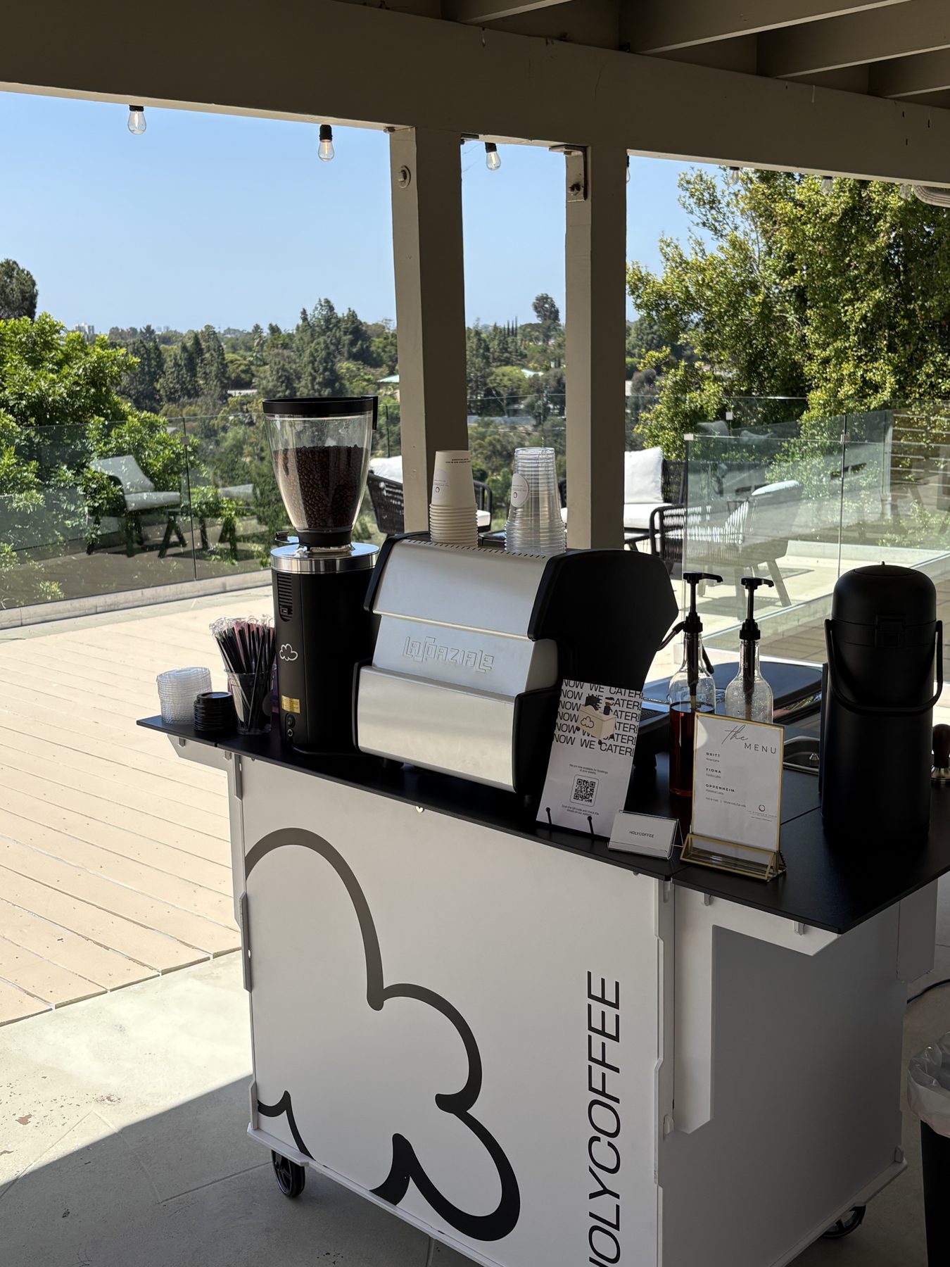 Holy Coffee cart on a rooftop terrace with a green hillside view