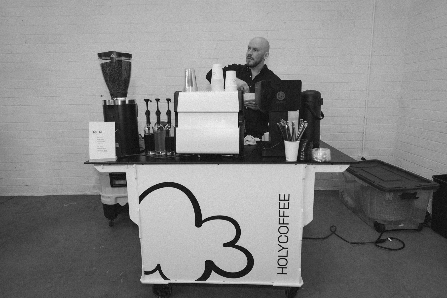 Black and white photo of the Holy Coffee cart with a barista at work