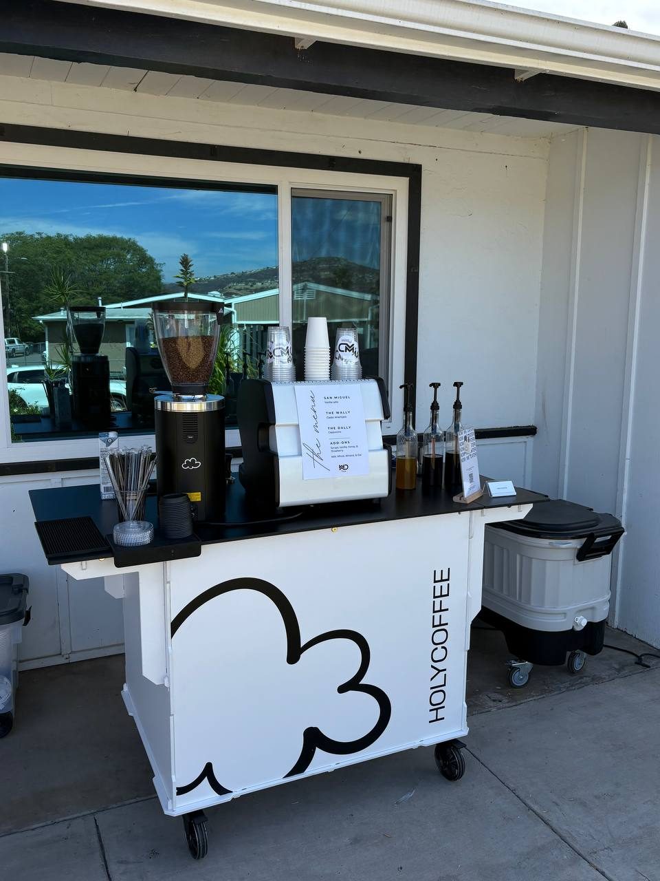 Holy Coffee cart set up outside a white building