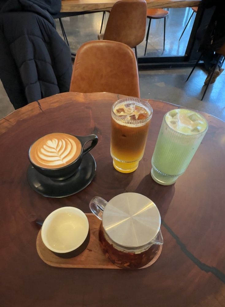 A latte, an espresso and orange drink, a matcha drink and tea on a wooden table