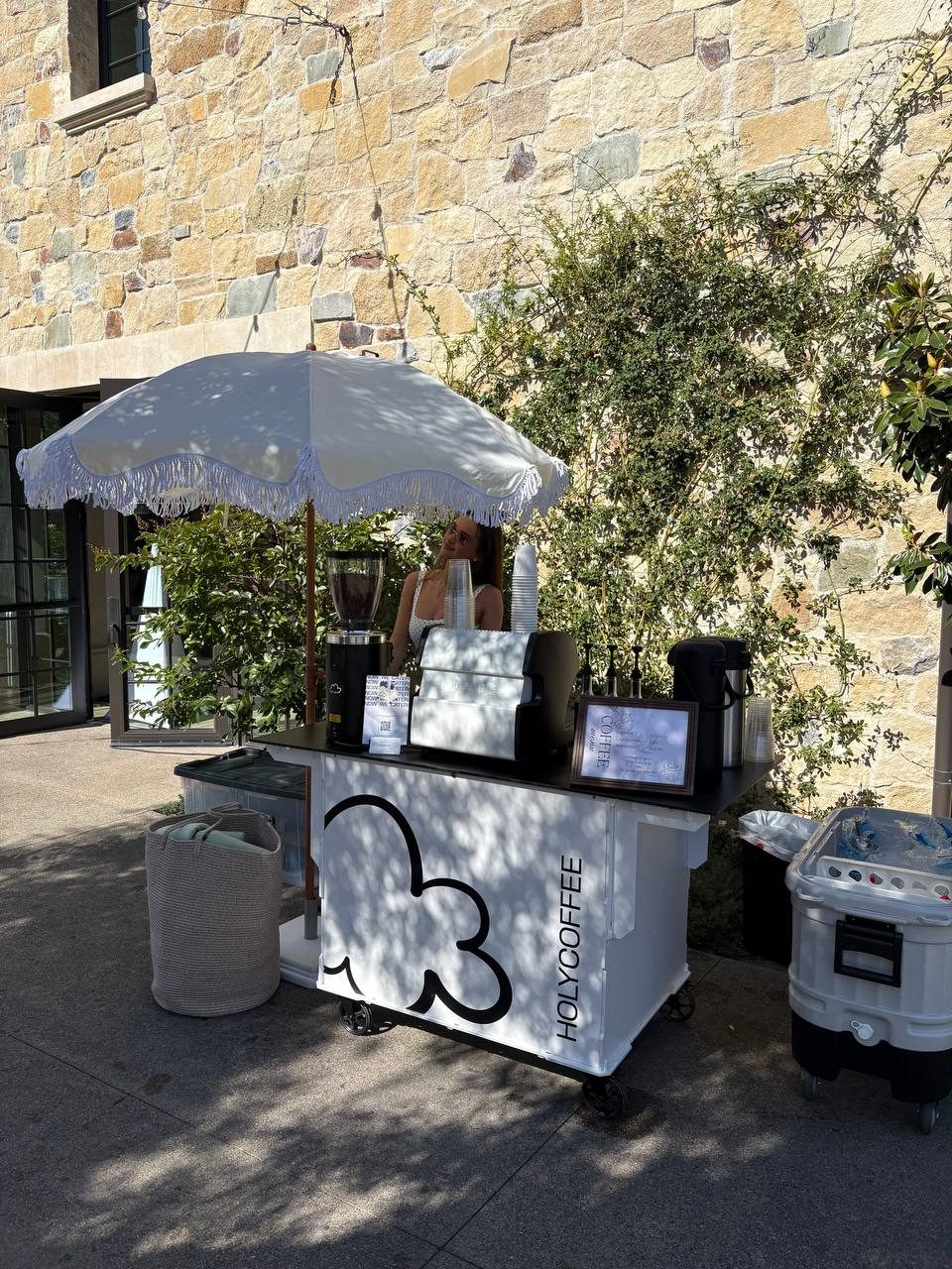 Holy Coffee cart on a stone patio under a white fringed umbrella