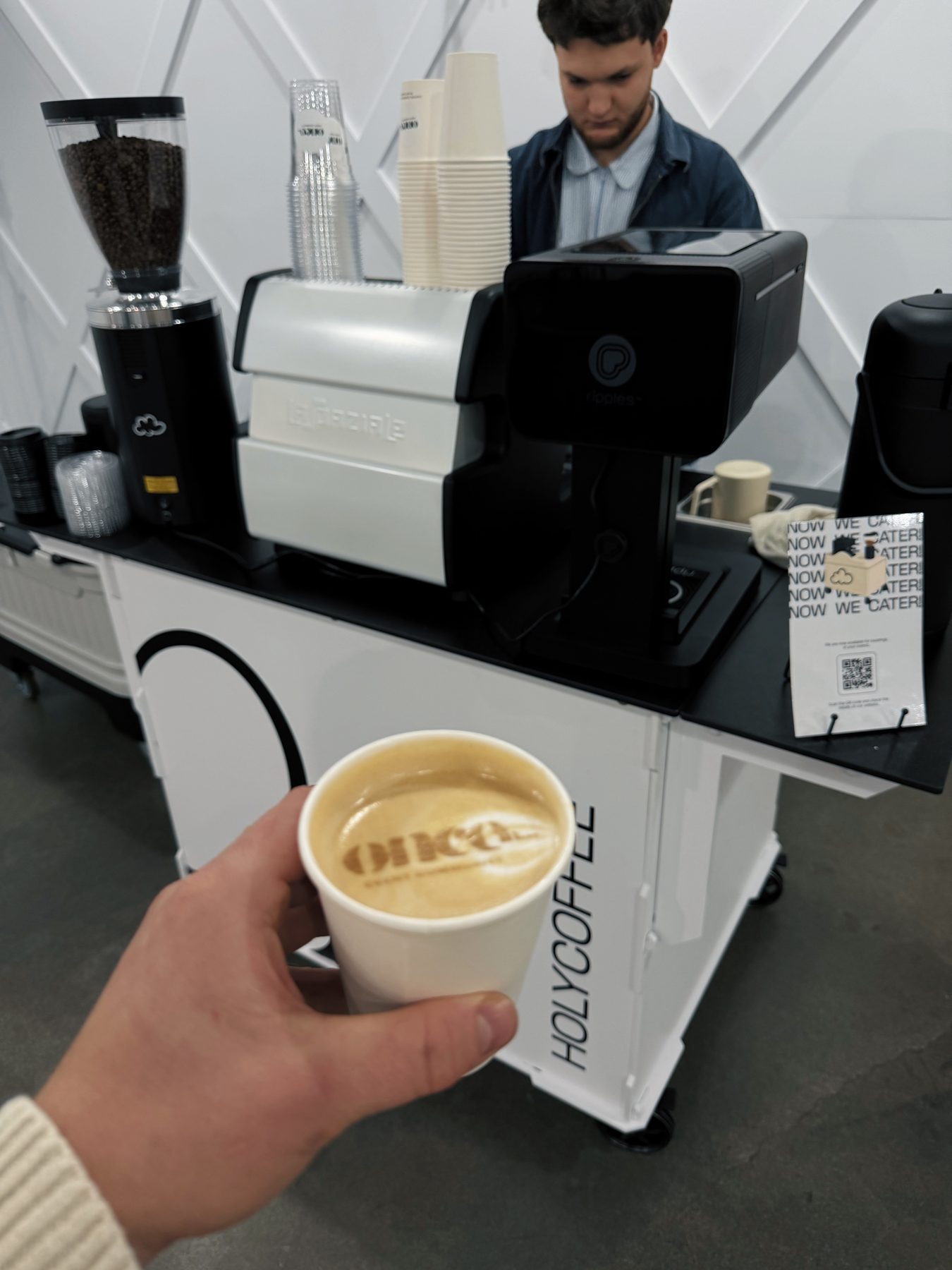 Latte with custom logo foam art held in front of the Holy Coffee cart