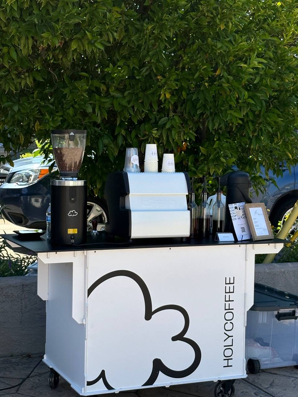 Holy Coffee cart outdoors under a leafy green tree