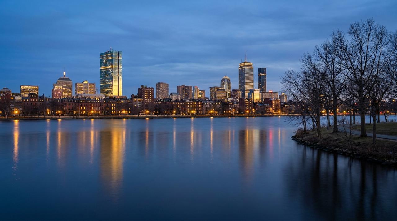 The Boston Back Bay skyline at blue hour across the Charles River, with the Prudential Tower and 200 Clarendon lit and the rowhouses of the Esplanade reflected in the water