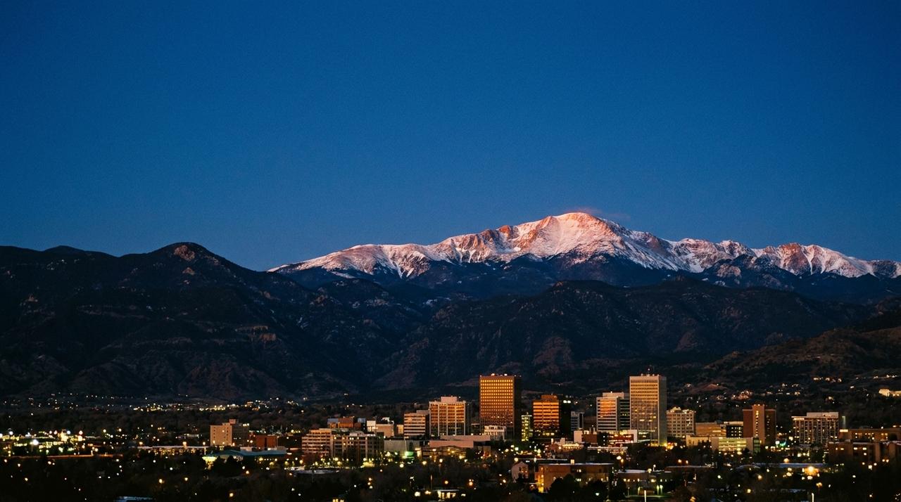 Downtown Colorado Springs at blue hour, with the office towers lit and snow-capped Pikes Peak glowing above the front range