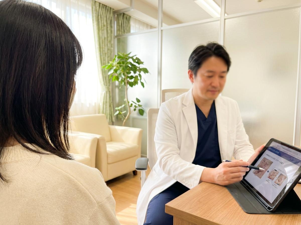 A plastic surgeon in a white coat walks a patient through a treatment plan on a tablet during a consultation
