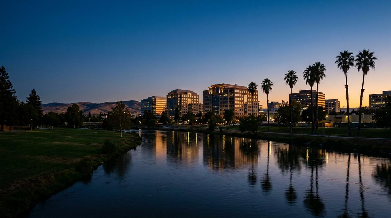 Downtown San Jose at blue hour across Guadalupe River Park, with the office towers lit, palm trees reflected in the river and the Diablo Range behind