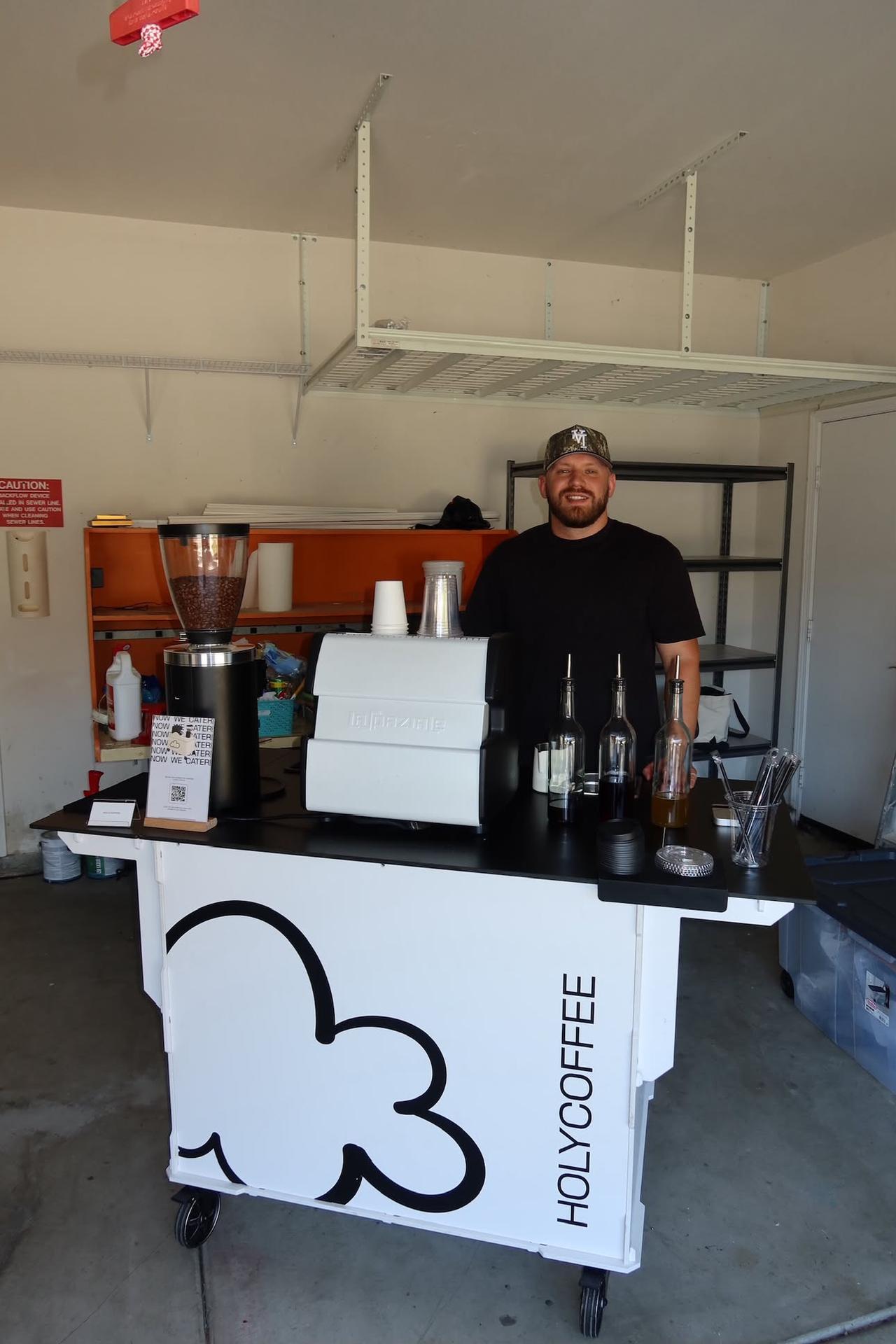 Smiling barista behind the white Holy Coffee cart with espresso machine and grinder