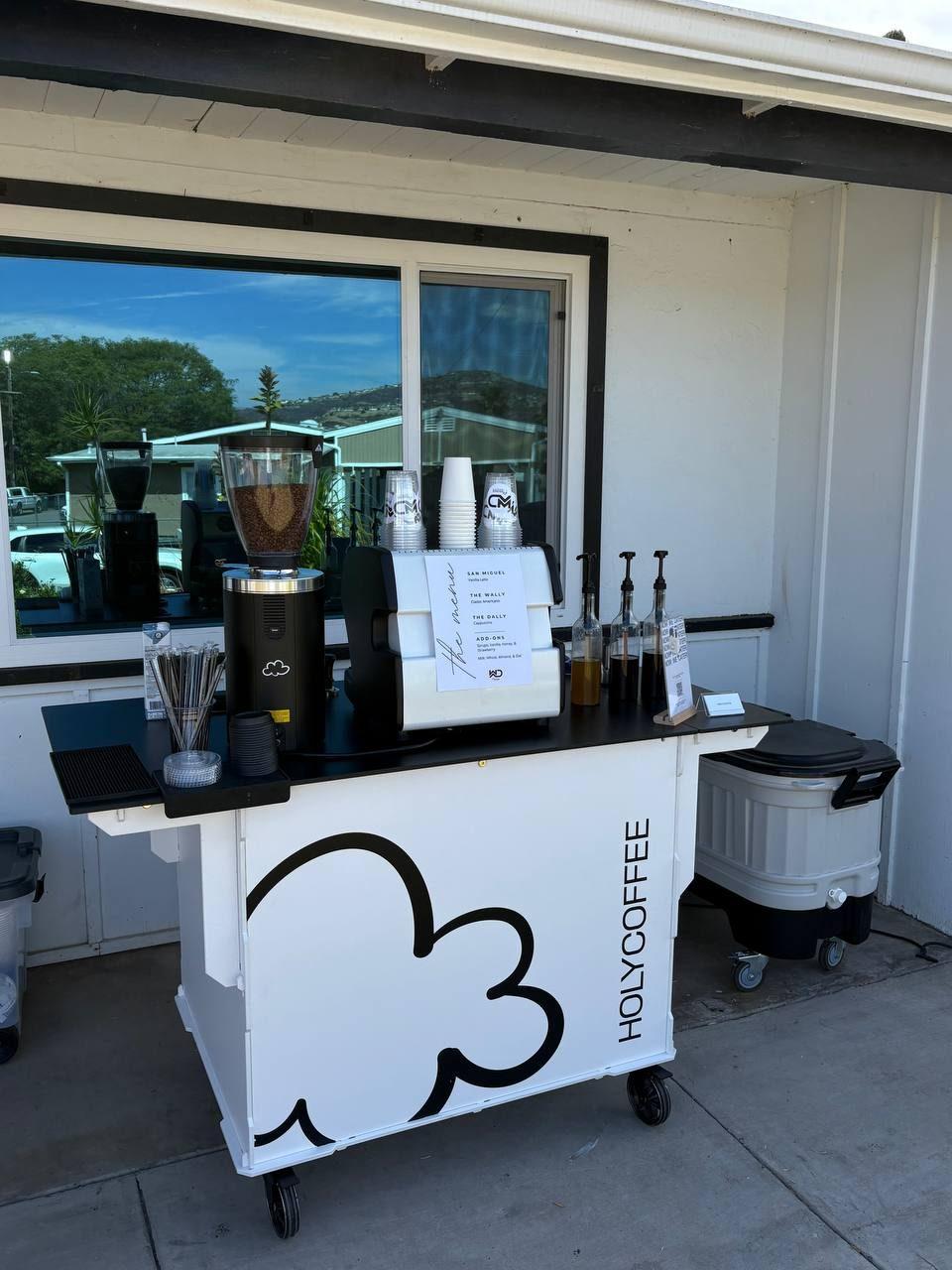 Holy Coffee cart set up outside a white building