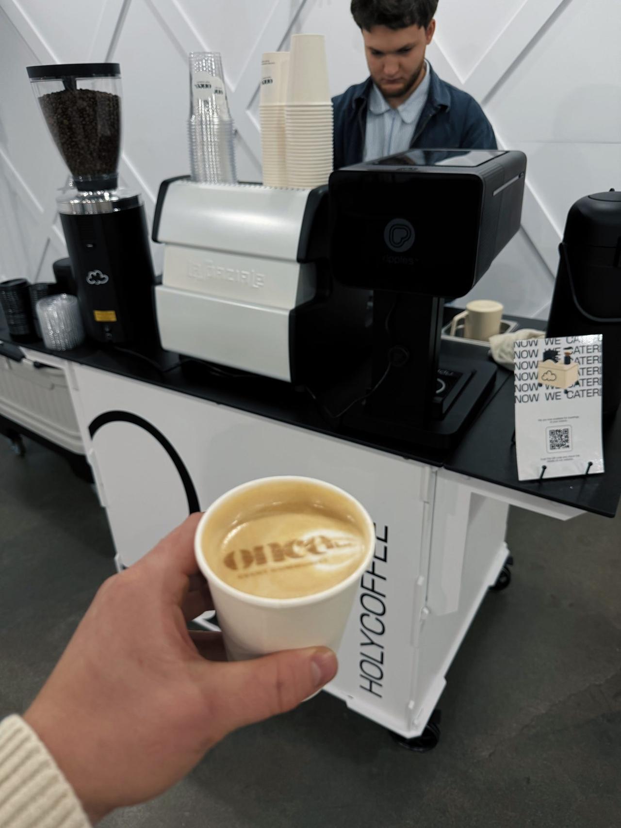 Latte with custom logo foam art held in front of the Holy Coffee cart