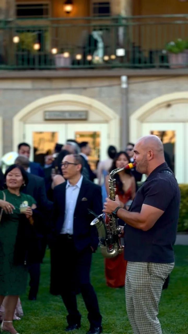 Igor playing sax among guests with drinks at an evening cocktail hour outside a venue