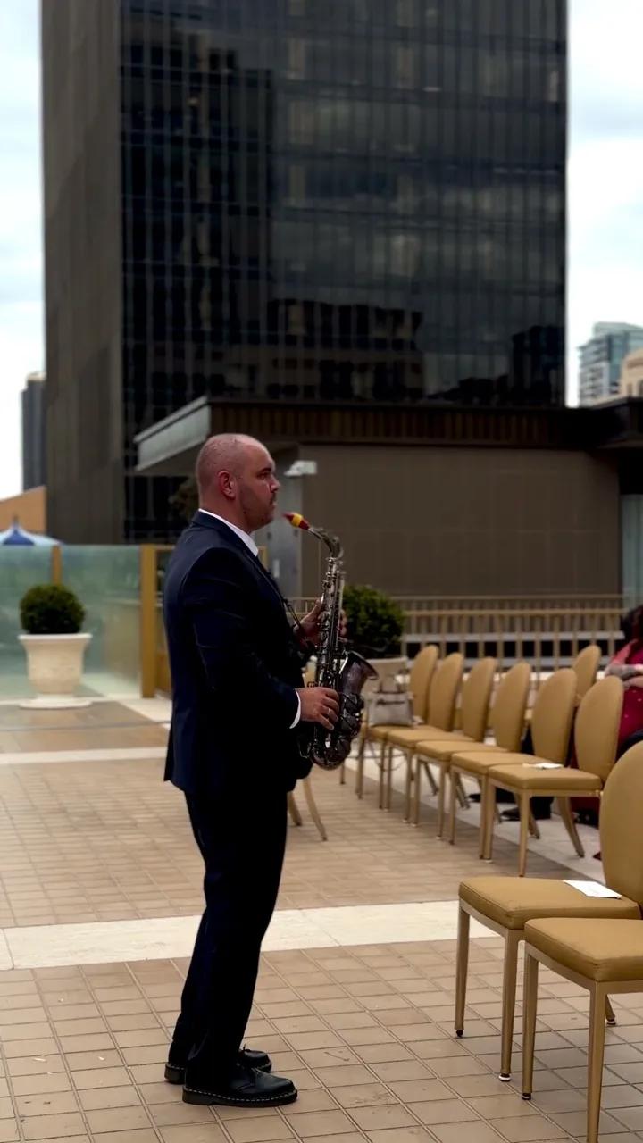 Igor in a black suit playing sax beside rows of ceremony chairs before a wedding