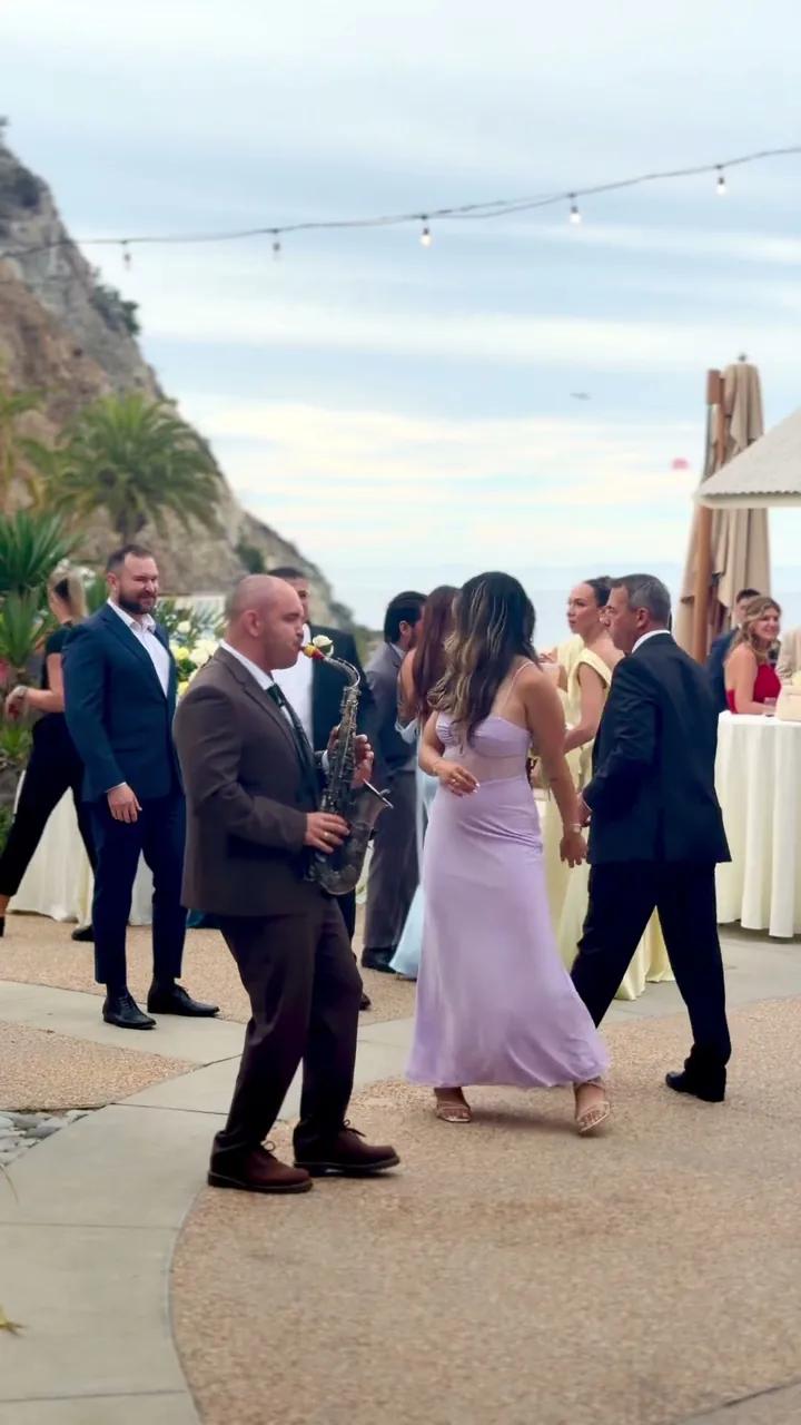 Igor in a brown suit playing sax among dancing guests on a terrace with string lights, San Diego wedding