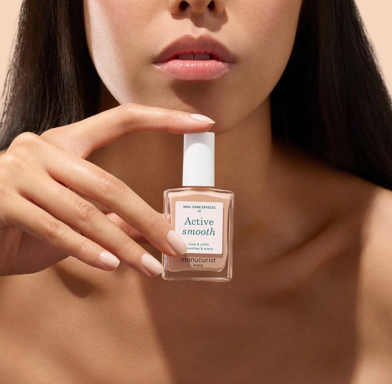 Hand with a clean natural manicure holding a bottle of Manucurist polish
