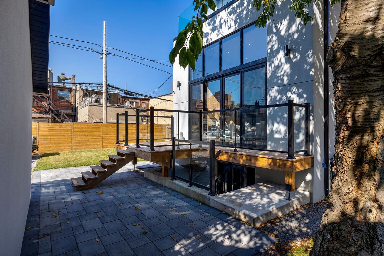 Rear of a modern KAV home with tall black framed windows, a glass-railed deck and a stone patio