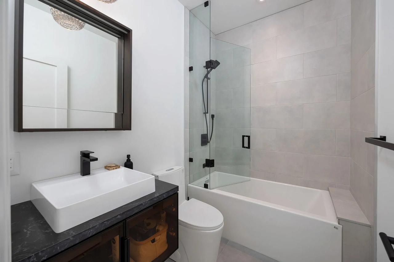 Bathroom with a black stone vanity, a white vessel sink, and a glass-screened tub and shower