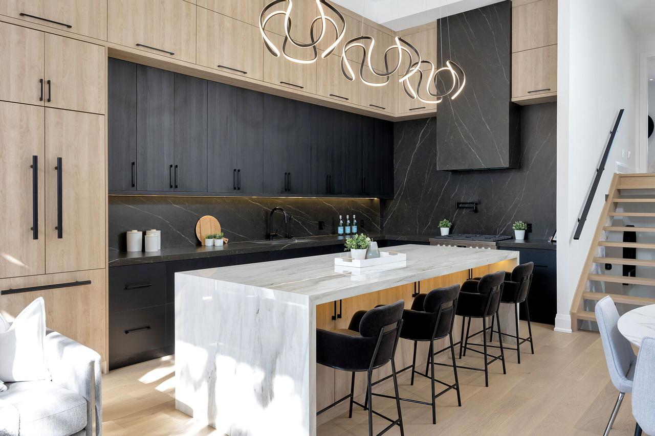 Kitchen with white oak and dark millwork to the ceiling, a marble waterfall island with black stools, and an open oak stair