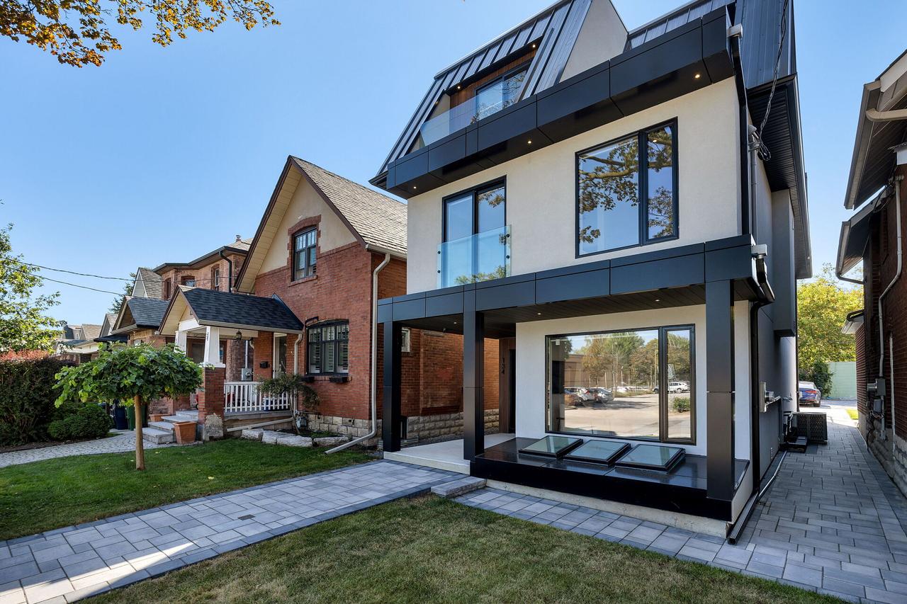 A modern three-storey KAV home with black framed windows, beside traditional brick houses on the same street