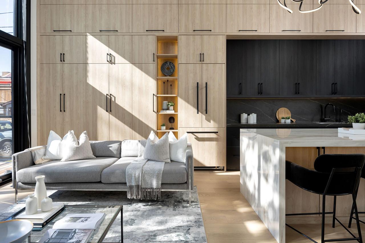 A KAV living room and kitchen with a full wall of light oak millwork, black cabinetry and a marble waterfall island